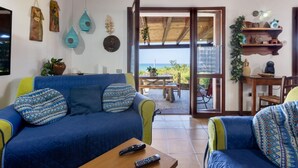 A living room with a sofa, a coffee table, and a view through a glass door to an outdoor patio. - GuestHost - Sea's Peace (Torre dei Corsari)