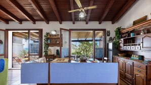 A dining area with a wooden ceiling, a ceiling fan, a table with a blue tablecloth, and a view through the open door. - GuestHost - Sea's Peace (Torre dei Corsari)