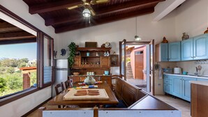 A kitchen with wooden cabinets, a dining table, and a view of greenery outside. - GuestHost - Sea's Peace (Torre dei Corsari)