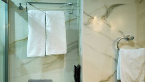 A bathroom with a glass-enclosed shower, a toilet, a marble-tiled wall, a towel rack, and a toilet paper holder.