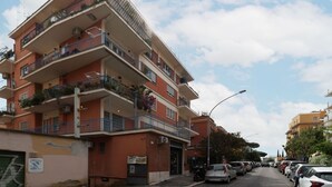 Un immeuble résidentiel à plusieurs étages, doté de balcons, donnant sur la rue et avec des voitures garées devant.