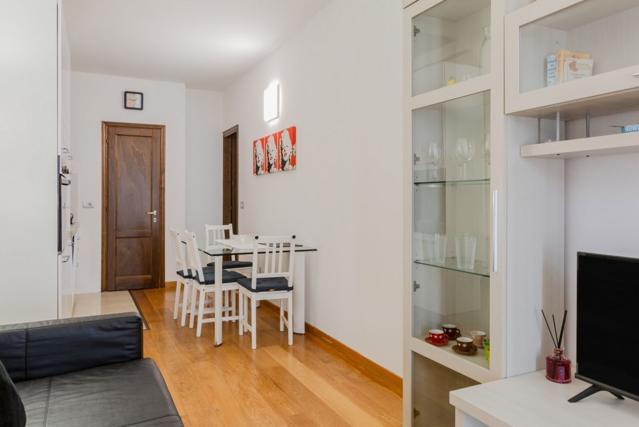 Un espace de vie compact comprenant un coin repas, un canapé, un téléviseur et une vitrine contenant divers objets.