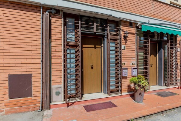 A brick building with a wooden door, metal gates, and a potted plant.