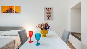 Et værelse med en seng, et bord med to glas, en vase med blomster og billedkunst på væggen.