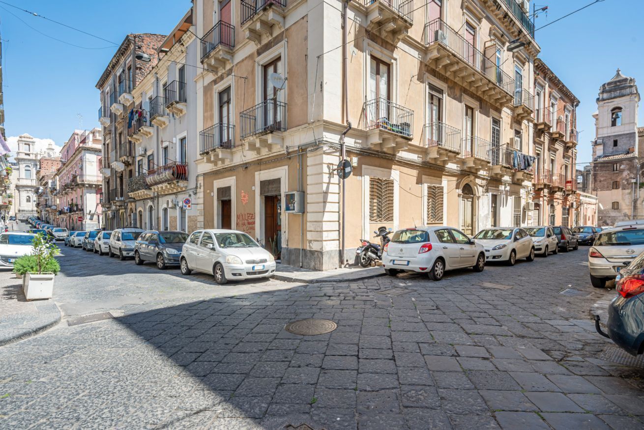 Calle adoquinada bordeada por vehículos estacionados y edificios históricos con balcones.