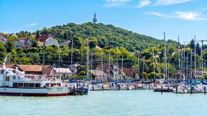 A marina with boats docked, a hill with trees in the background, and a clear sky. - Sunset Resort 409 With Pool (Fonyod)
