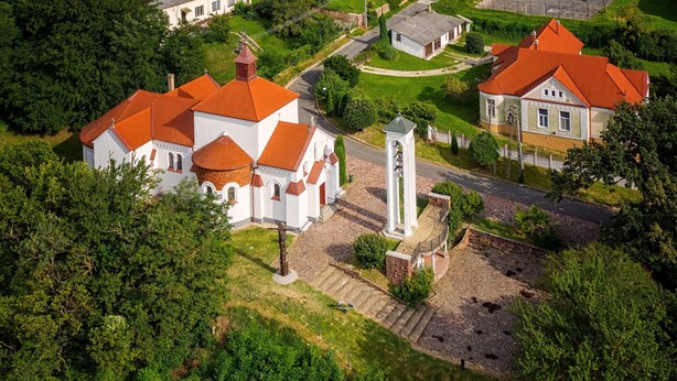 Luchtbeeld van een kerk met een klokkentoren, omringd door groen en omliggende gebouwen.