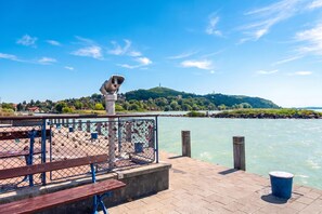 On aperçoit clairement une promenade en bord de mer, avec un télescope, des bancs et une rambarde donnant sur une étendue d'eau calme.