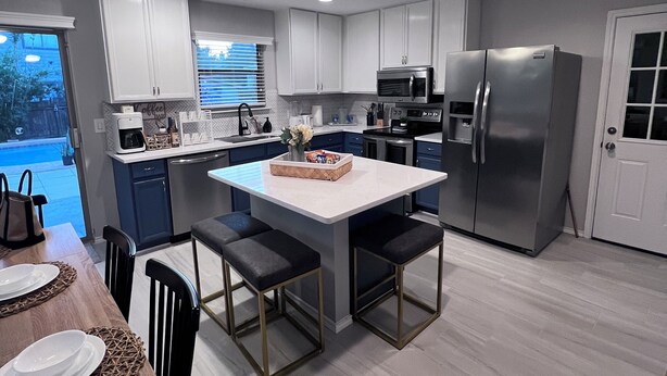 A modern kitchen with white cabinets, a stainless steel refrigerator, and a dining area with a wooden table and chairs. - Tulum House in Austin Tx (Austin)
