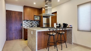 A kitchen with wooden cabinets, a stainless steel range hood, a granite countertop, and two bar stools. - 2BD, 2BA Luxury Penthouse with Private Rooftop in Cabo.  LOTS OF BEACH GEARS! (Cabo San Lucas)