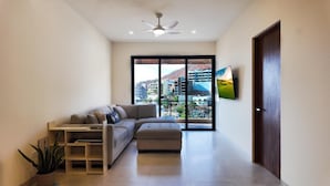 A modern living room with a sofa, ottoman, and a flat-screen TV mounted on the wall. - 2BD, 2BA Luxury Penthouse with Private Rooftop in Cabo.  LOTS OF BEACH GEARS! (Cabo San Lucas)