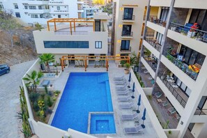 A rooftop pool with sun loungers and a pergola, surrounded by a landscaped garden.