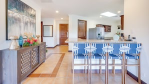 Una cocina moderna con barra, que incluye una isla grande con taburetes, un refrigerador y un jarrón decorativo con flores.