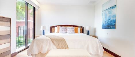 A bedroom with a bed, bedside lamps, a bench, a ceiling fan, and a large window.