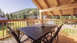 Una terraza de madera con una mesa y sillas, con vistas a un paisaje montañoso.