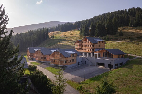 A modern building with multiple wooden structures and a large central building, surrounded by a grassy landscape and trees.