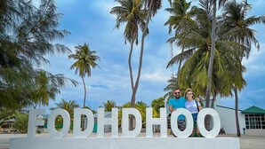 Ein Schild mit dem Schriftzug "FODIHOO" in großen Buchstaben, umgeben von Palmen und einem wolkenlosen Himmel.