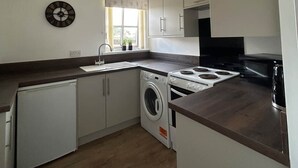 Cocina compacta con lavadora, lavamanos y ventana con cortinas.