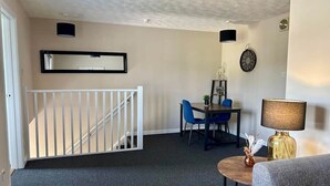 Una sala de estar con una escalera, un comedor con sillas, una mesa, una lámpara y un reloj en la pared.