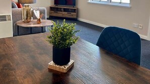Una sala moderna con una mesa de comedor de madera, una planta en maceta, un televisor sobre un mueble de madera y una ventana con persianas.