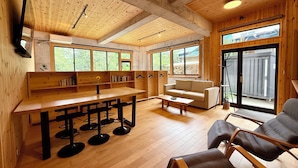 A wooden interior with a dining area, sofa, and large windows.