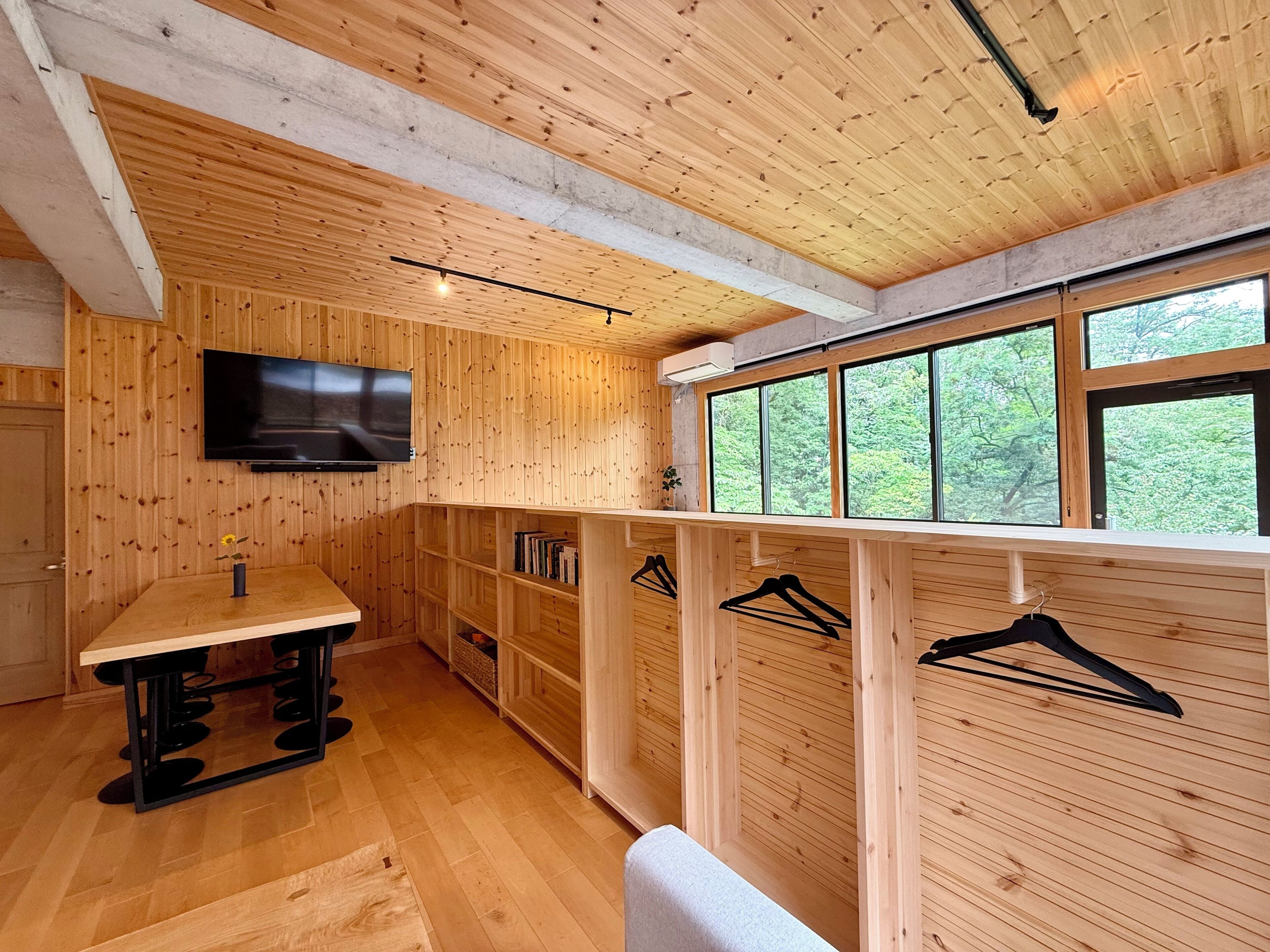 A wooden interior with a TV, wooden shelves, a table, and a bench.
