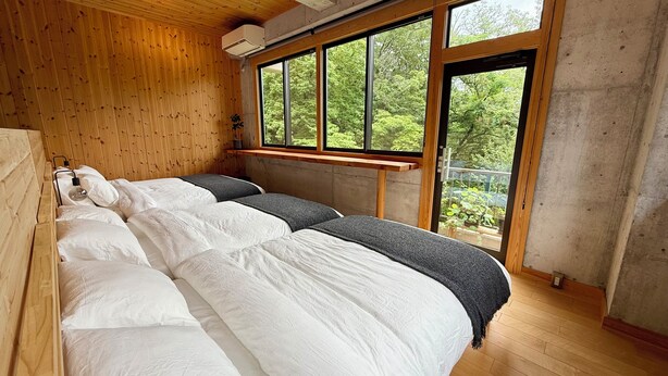A room with two beds, wooden walls, a large window, and a view of greenery.