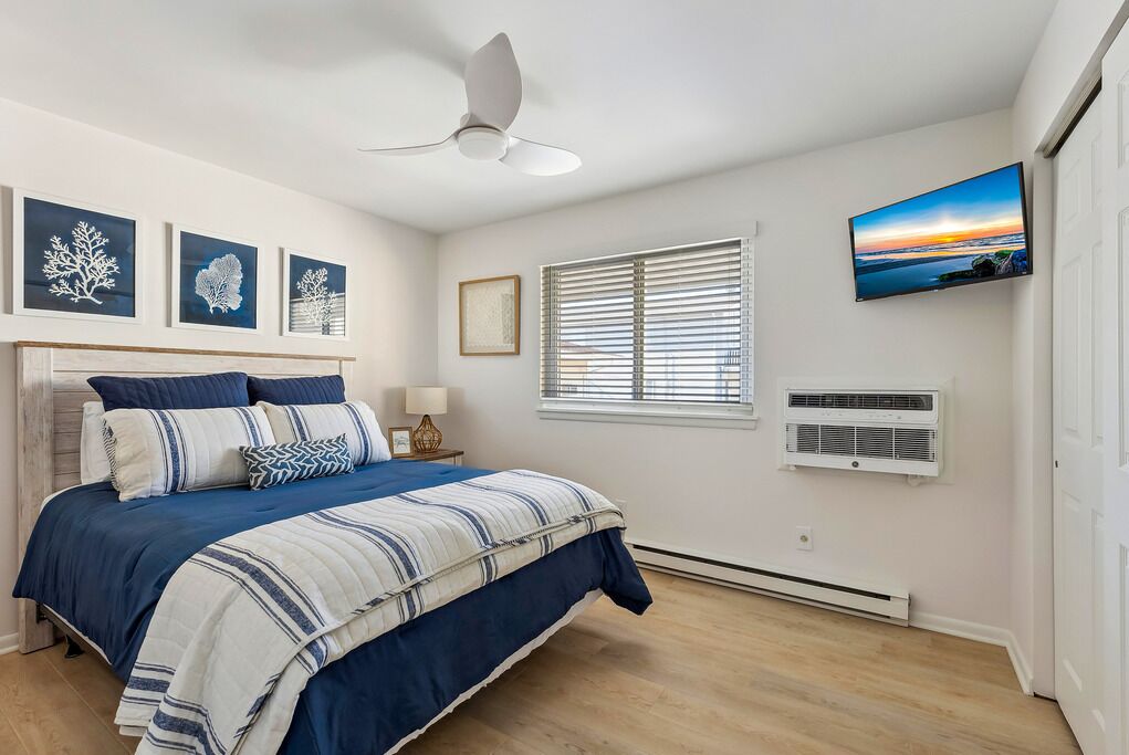 Een slaapkamer met een bed, plafondventilator, kunstwerk, raam, airconditioning en een televisie.