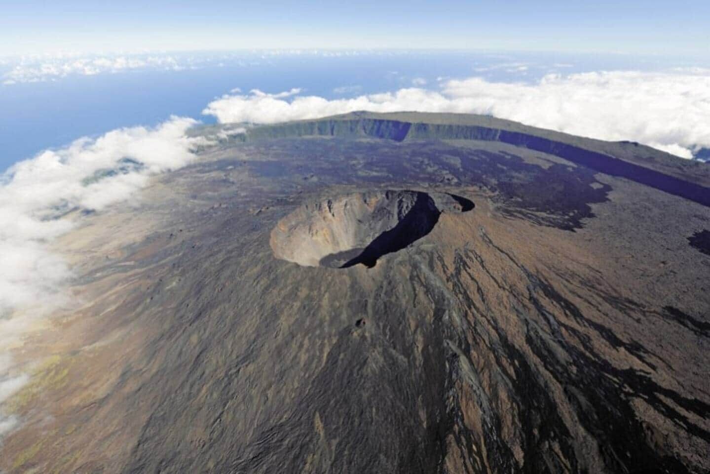 A volcanic crater with a rugged terrain and a view of the ocean and clouds.