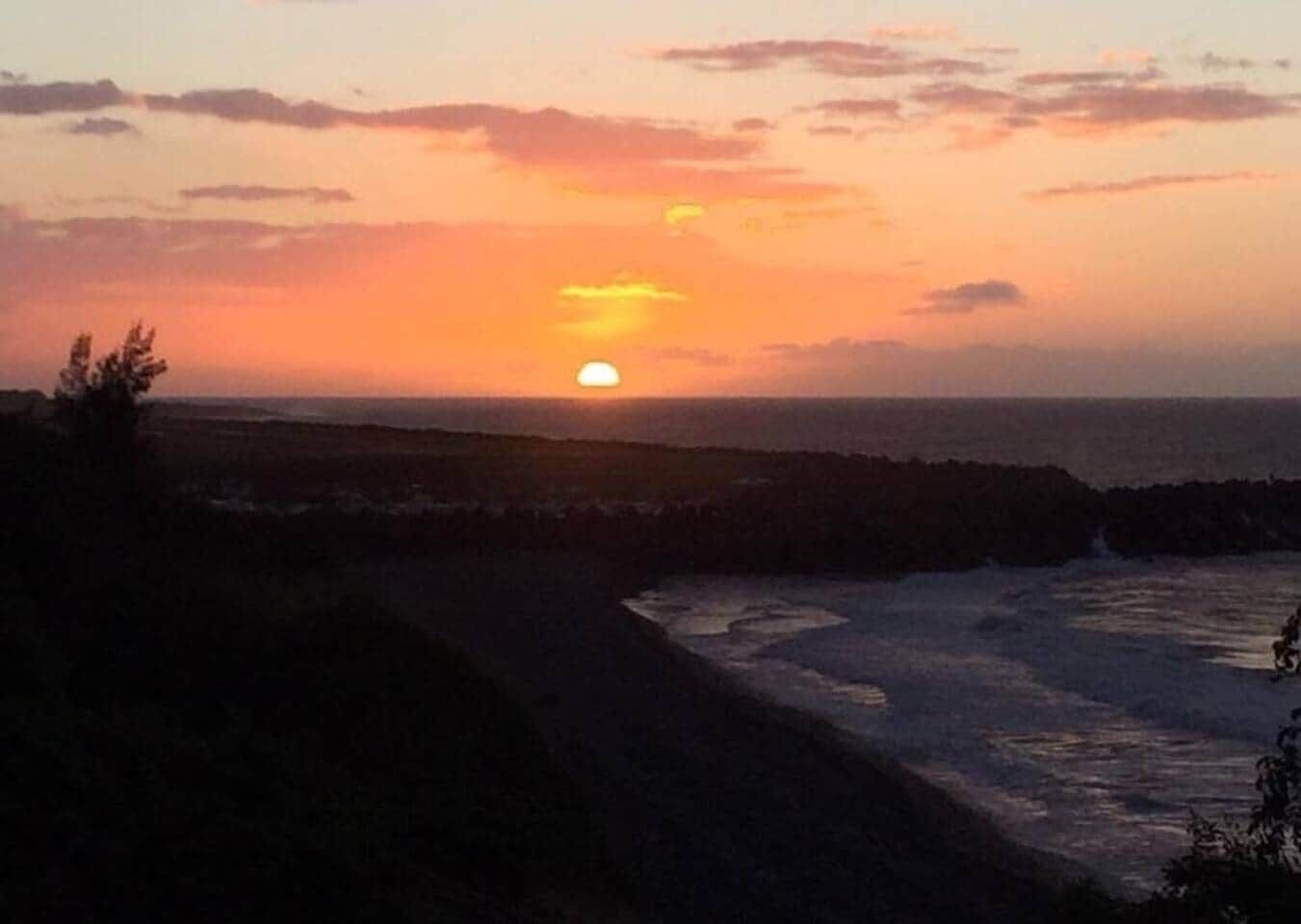 A sunset over a coastal landscape with rocky terrain and a path leading to the water.