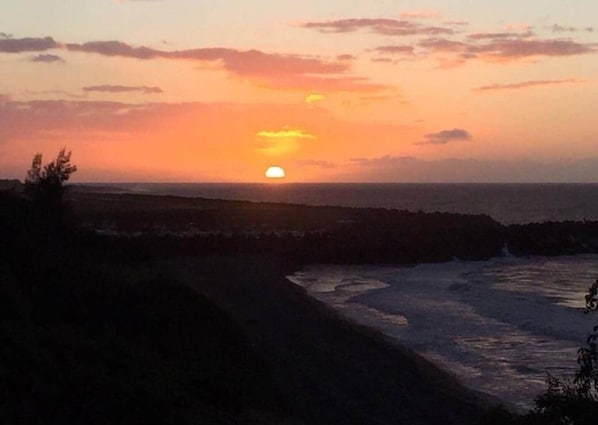 A sunset over a coastal landscape with rocky terrain and a path leading to the water.