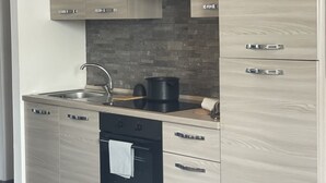 Une cuisine moderne avec des meubles de couleur bois clair, un four noir, un évier en acier inoxydable et une casserole noire posée sur le plan de travail.