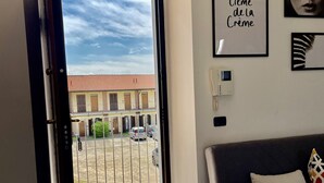 Une pièce avec un canapé gris, une porte donnant sur un balcon extérieur et un mur orné d’un tableau encadré et d’une enseigne.