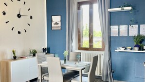 Un espace repas moderne avec une table blanche, quatre chaises et une horloge au mur.