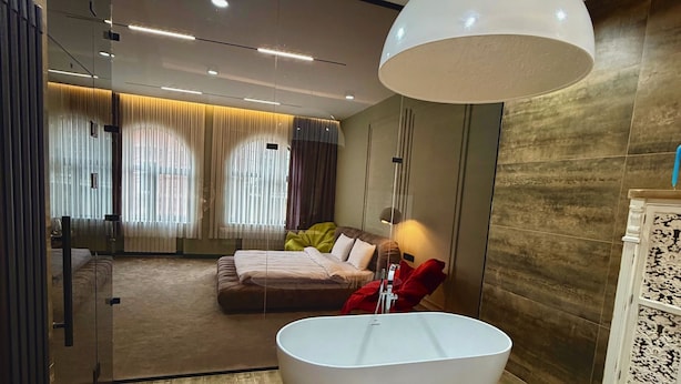 A modern bathroom with a freestanding bathtub, a large pendant light, and a glass partition separating the bathroom from the bedroom. - Casa Blu (Tbilisi)