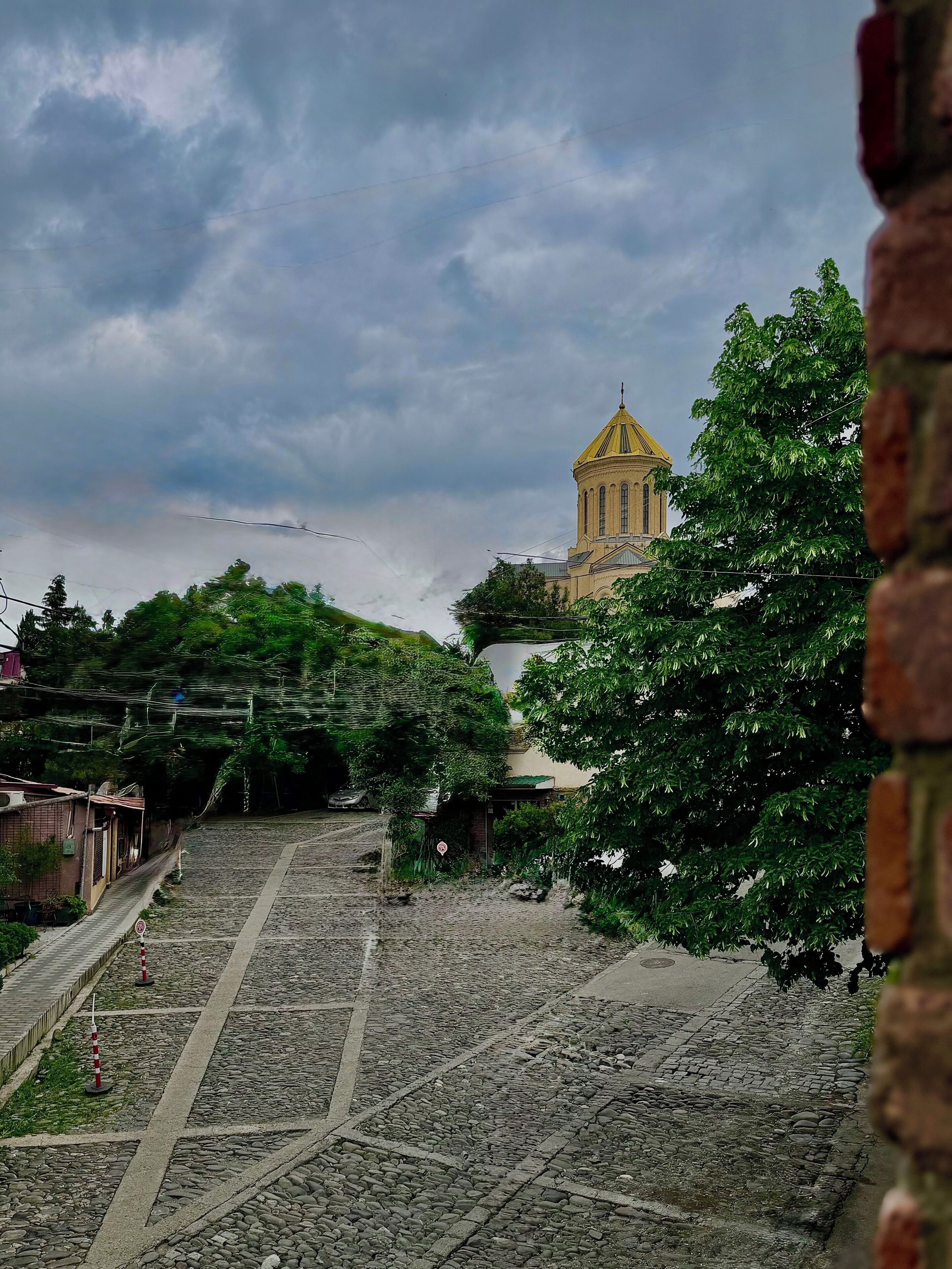 A cobblestone pathway leading to a building with a yellow dome, surrounded by greenery.