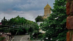 A cobblestone pathway leading to a building with a yellow dome, surrounded by greenery. - Casa Blu (Tbilisi)