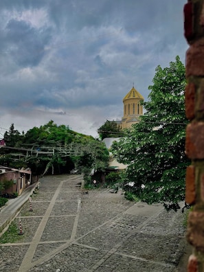 A cobblestone pathway leading to a building with a yellow dome, surrounded by greenery. - Casa Blu (Tbilisi)
