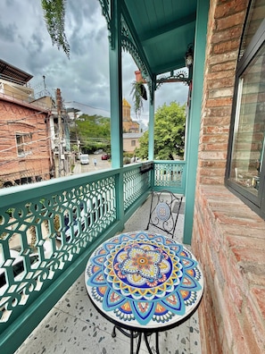Un balcon avec une table à motifs, une rambarde verte et une vue sur un bâtiment surmonté d’un dôme jaune.