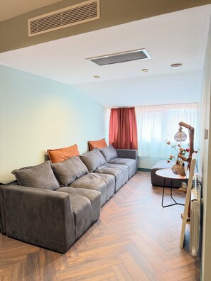 A living room with a sectional sofa, a small round table, and a radiator. - Casa Blu (Tbilisi)