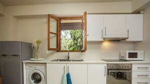 A compact kitchen with a washing machine, a microwave, and an oven. - Art House (Rhodes)