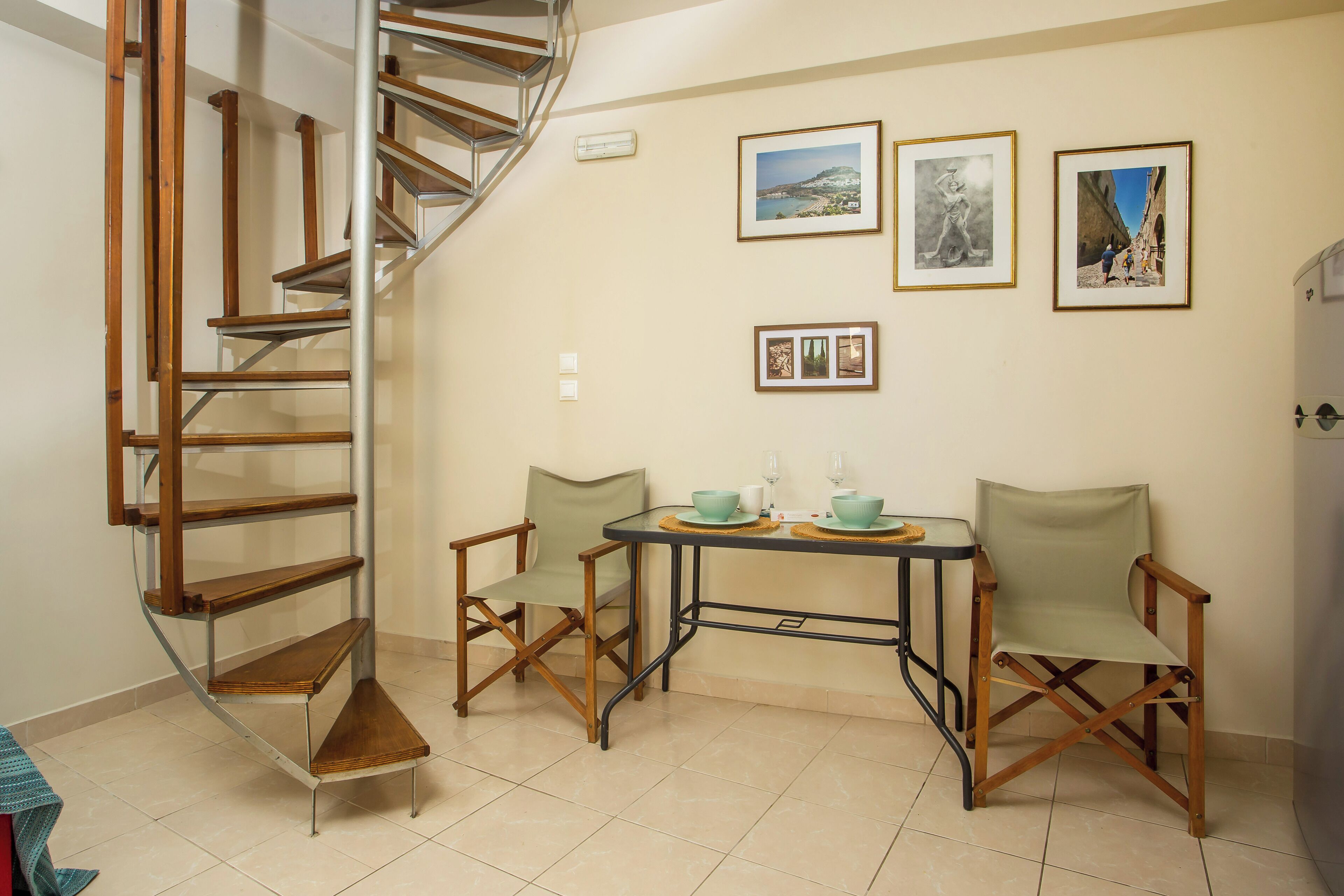 Una habitación con una escalera de caracol, una mesa de comedor con dos sillas y tres cuadros en la pared.