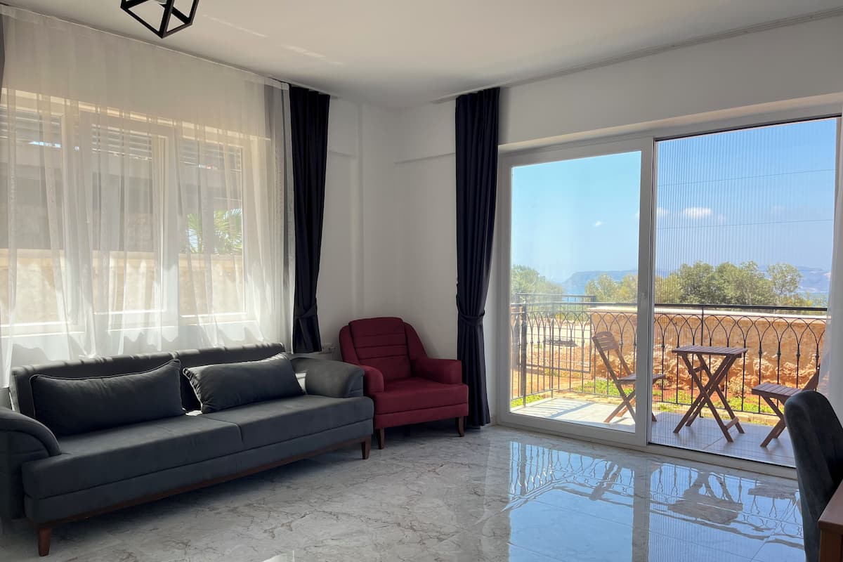 A modern living room with a grey sofa, a red armchair, and a balcony with outdoor furniture.