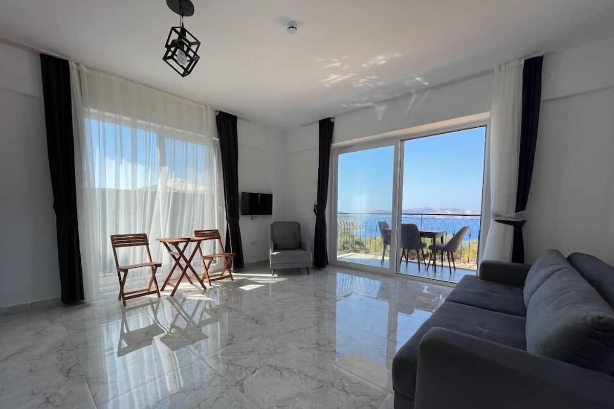 A spacious living room with a large sofa, a dining table with chairs, and a balcony with a view of the sea.