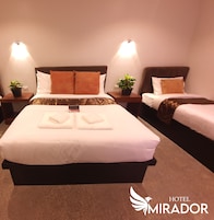 A hotel room with a large bed, two bedside tables with lamps, a potted plant, and a sign indicating the hotel name.