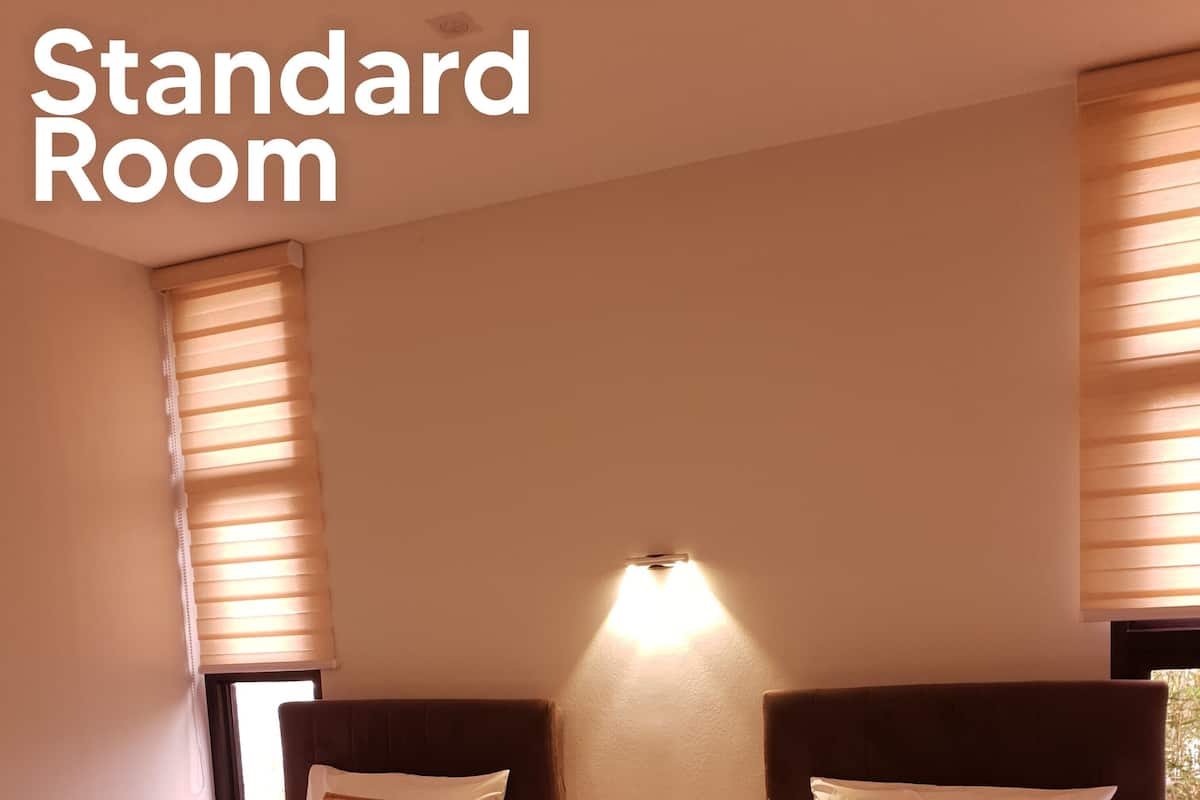 Habitación estándar con dos camas, cada una con cabecero, mesitas de noche e iluminación de pared.