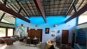 A spacious living area with a high ceiling, a large window, and a blue accent wall. There are several seating options, including a sofa and a chair. - AMAZON HOME AND JUNGLE TRIPS (Manaus)