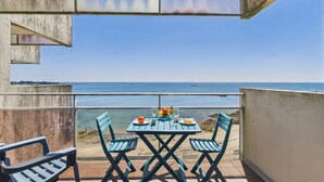 A balcony with a table and chairs overlooking a beach and the sea.