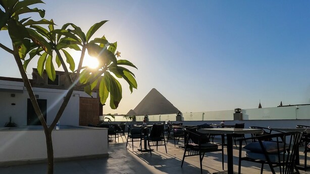 A rooftop terrace with outdoor seating, a pyramid-shaped structure, and a view of the city skyline.
