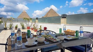 A table set with food and drinks on a rooftop terrace with views of pyramids.